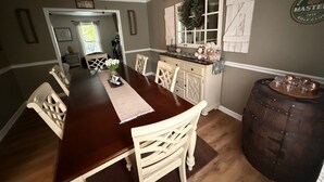 A dining area with a wooden table, white chairs, a ceiling fan, and a decorative wreath on a window. - Charming Cape Cod Style Home-Masters Rental (Augusta)
