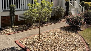 A two-story building with a white exterior, a covered porch with white railings, and a small garden area with pebbles and plants. - Charming Cape Cod Style Home-Masters Rental (Augusta)