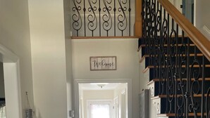 A hallway with a wooden floor, a white door at the end, and a 'Welcome' sign above the door. - Charming Cape Cod Style Home-Masters Rental (Augusta)