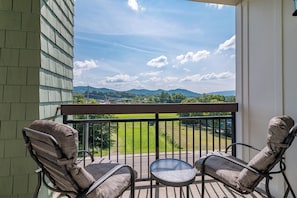 A balcony with two chairs and a small table, overlooking a green landscape and mountains. - Luxury Condo in Pigeon Forge (Pigeon Forge)