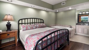 A bedroom with a bed, bedside table, lamp, and a bathroom with a bathtub and sink.