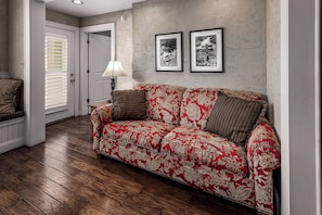 A living room with a patterned sofa, wooden flooring, a door with blinds, and two framed pictures on the wall. - Luxury Condo in Pigeon Forge (Pigeon Forge)