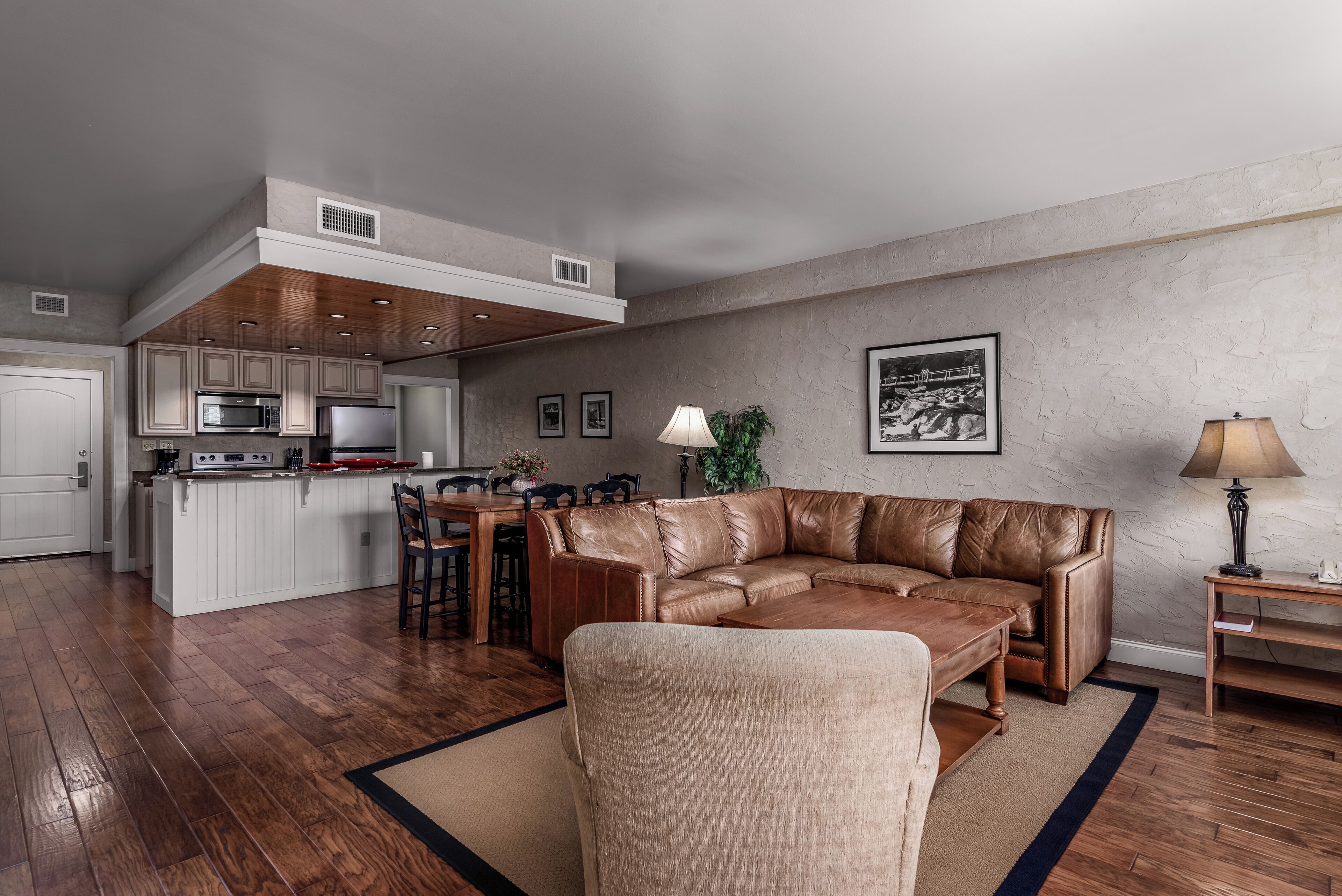Una sala moderna con un sofá de cuero, una mesa de centro de madera y un comedor con una cocina al fondo.