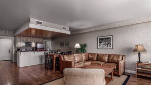 A modern living room with a leather sofa, wooden coffee table, and a dining area with a kitchen in the background.