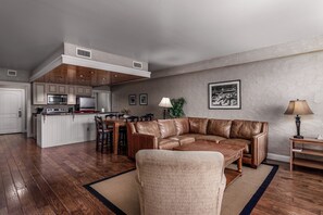 A modern living room with a leather sofa, wooden coffee table, and a dining area with a kitchen in the background. - Luxury Condo in Pigeon Forge (Pigeon Forge)