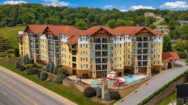 A multi-story hotel with balconies, a swimming pool, and a landscaped area with trees.