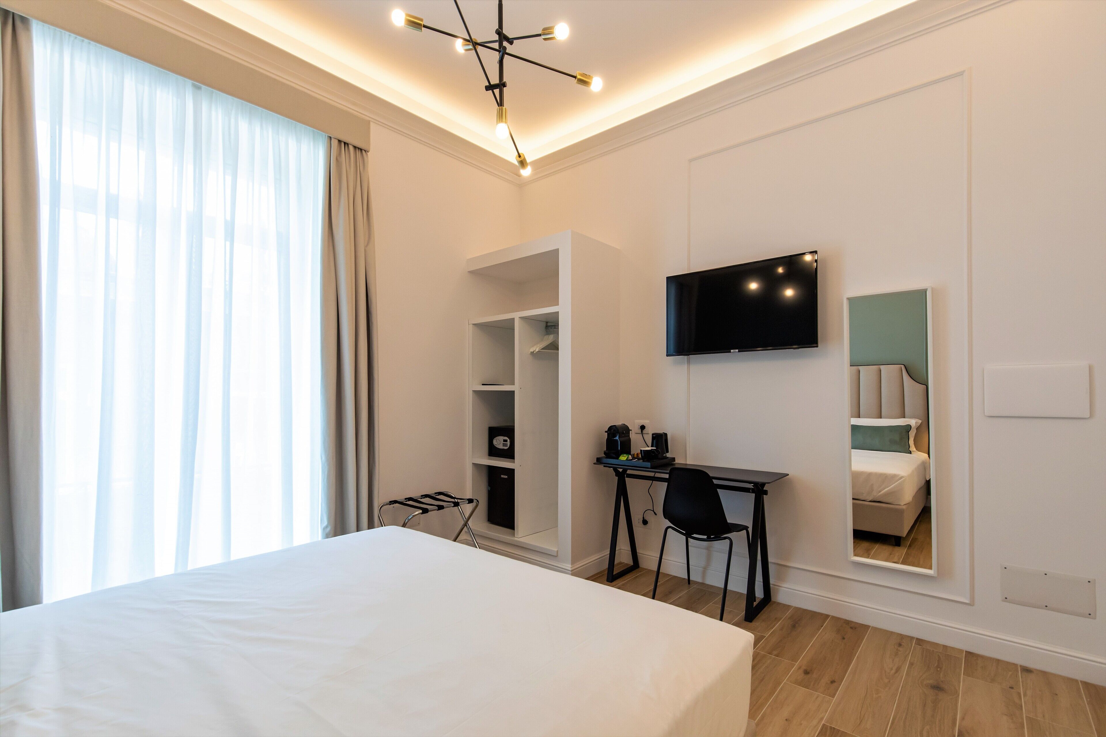 Una habitación de hotel moderna con una cama grande, un escritorio, una silla, un televisor y estanterías integradas.