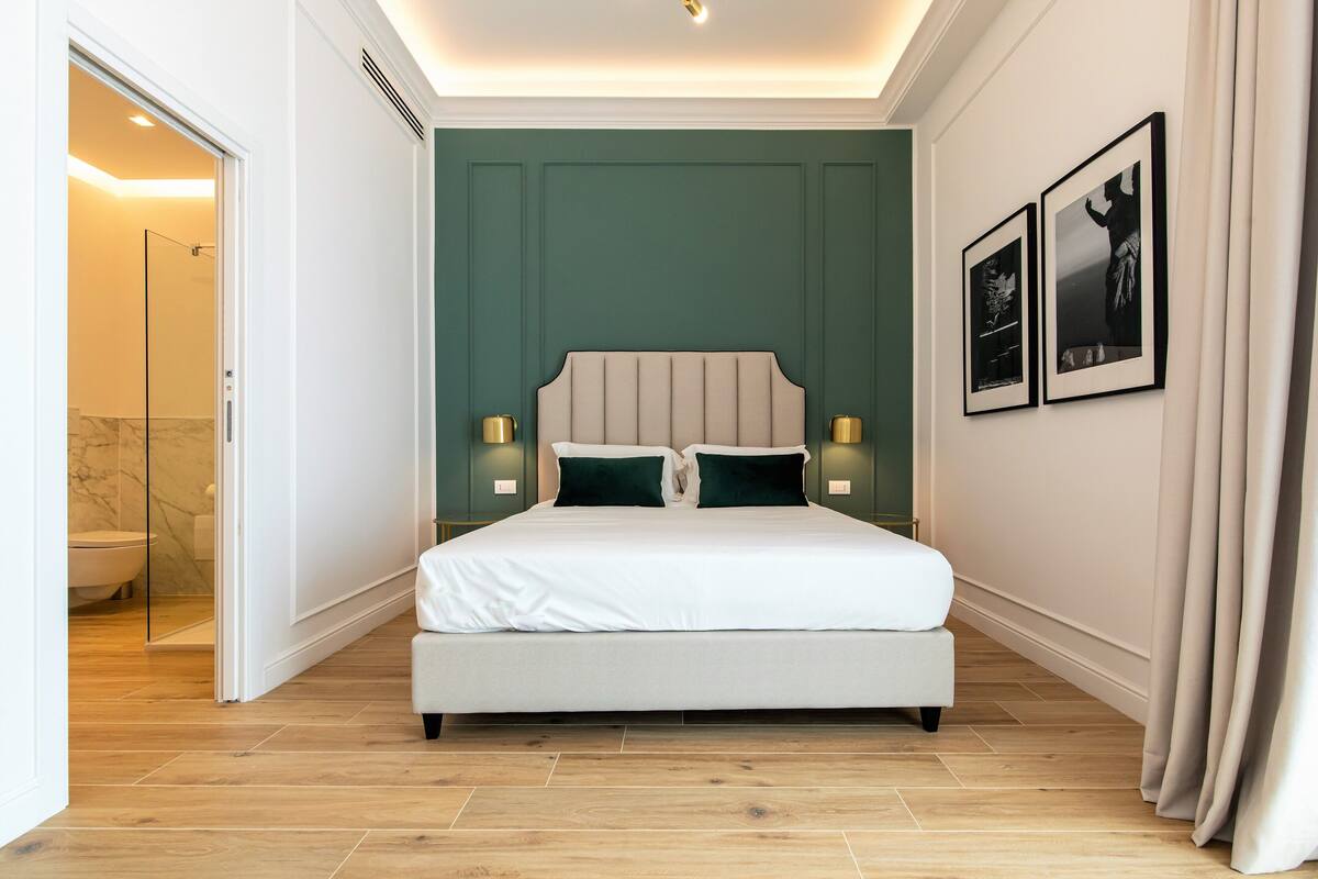 A modern bedroom with a large bed, a glass shower, and a green accent wall.