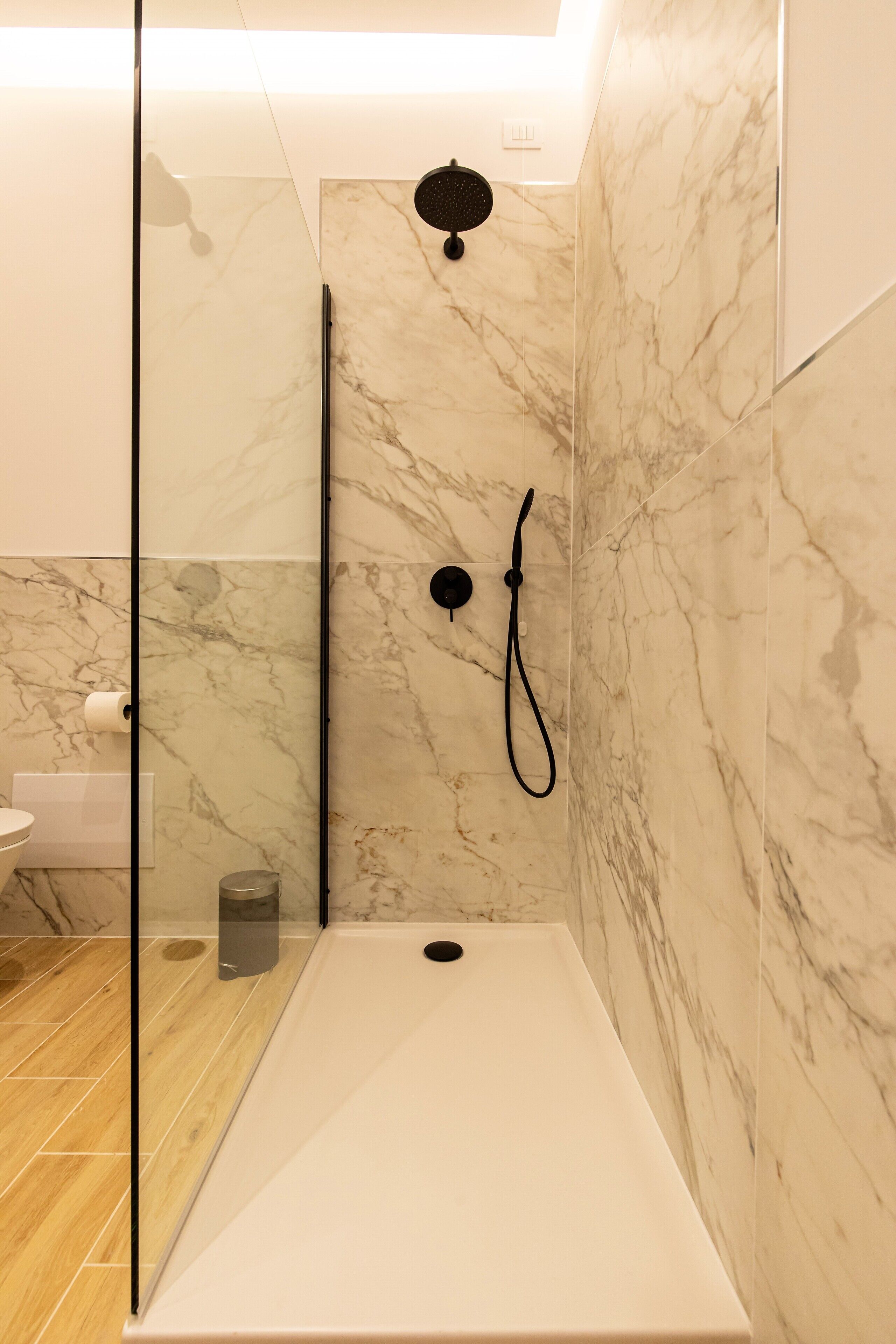 Un baño moderno con ducha de vidrio, paredes de mármol y suelo de madera.