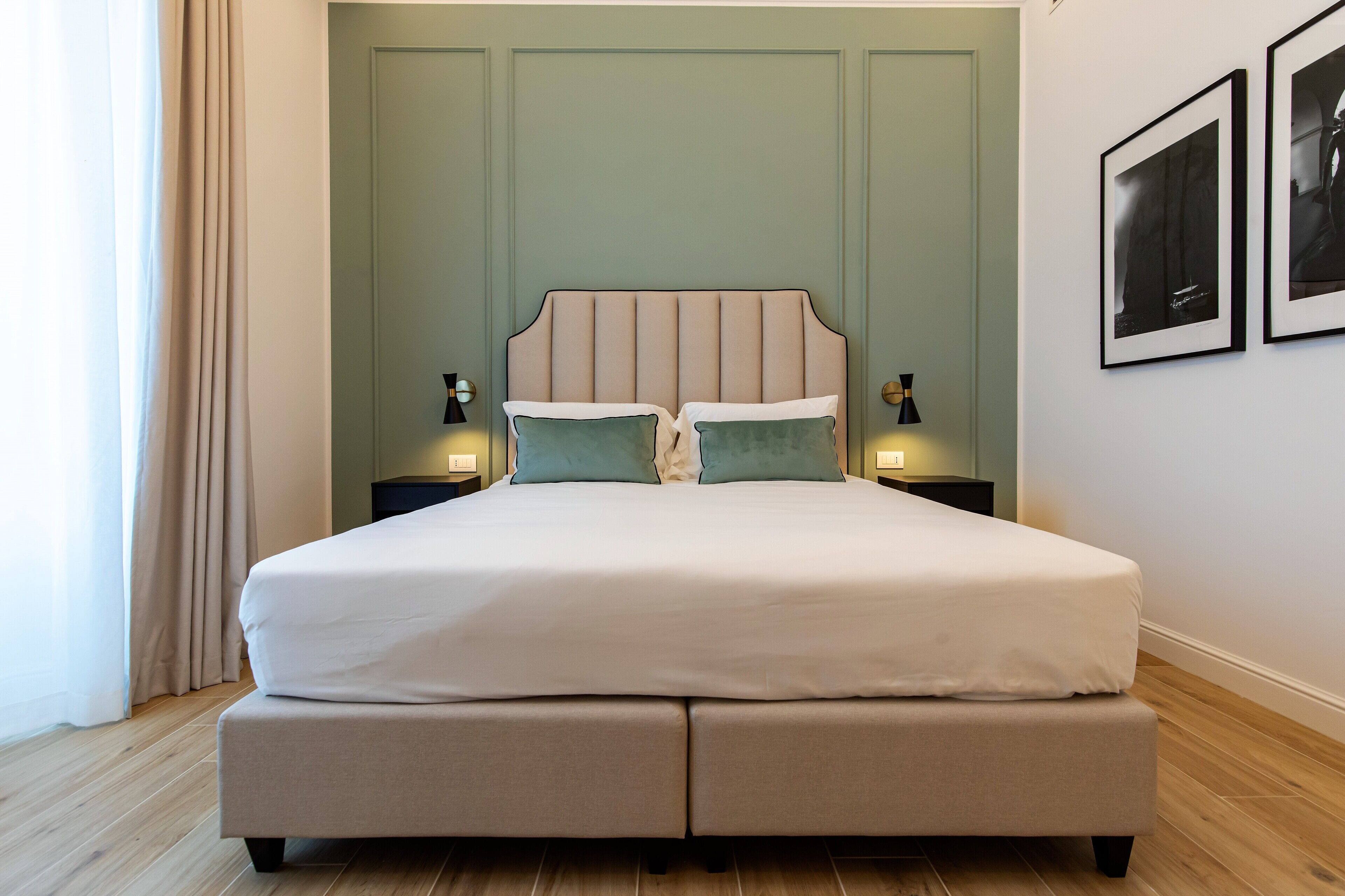 Una cama bien hecha con cabecera, dos mesitas de noche con lámparas y suelo de madera.