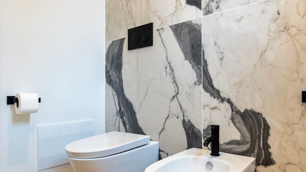 A modern bathroom with a marble backsplash, a white toilet, and a pedestal sink. - Unico Relais (Naples)