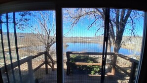 A view through a window with a wooden deck overlooking a lake and trees.