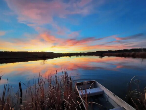 A calm body of water reflecting a sunset sky with a boat docked at the edge.
