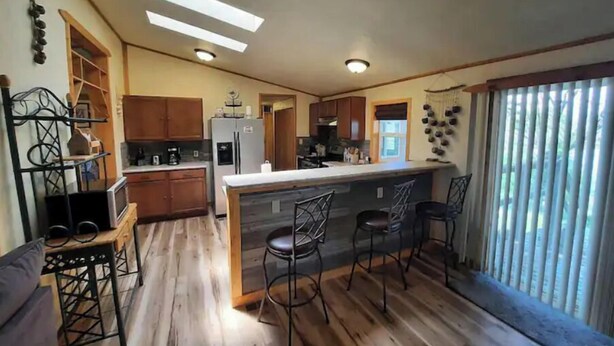 A kitchen with wooden flooring, a central island with bar stools, and a refrigerator.
