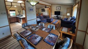 A spacious living area with a wooden dining table, blue upholstered sofas, and a ceiling fan.
