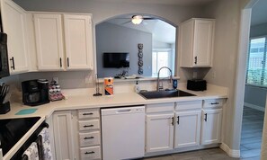 A kitchen with white cabinets, a dishwasher, a coffee maker, and a sink. - Peoria 3 Bedroom 2 bath Home with 2 Car Garage and Community Pool. (Peoria)