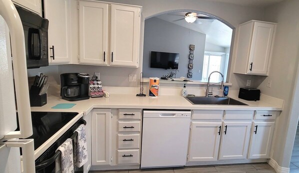 A kitchen with white cabinets, a black microwave, a coffee maker, and a sink. - Peoria 3 Bedroom 2 bath Home with 2 Car Garage and Community Pool. (Peoria)