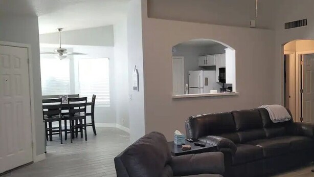 Uma sala de estar com um sofá de couro escuro, uma mesinha lateral e um espaço de refeições com mesa e cadeiras.