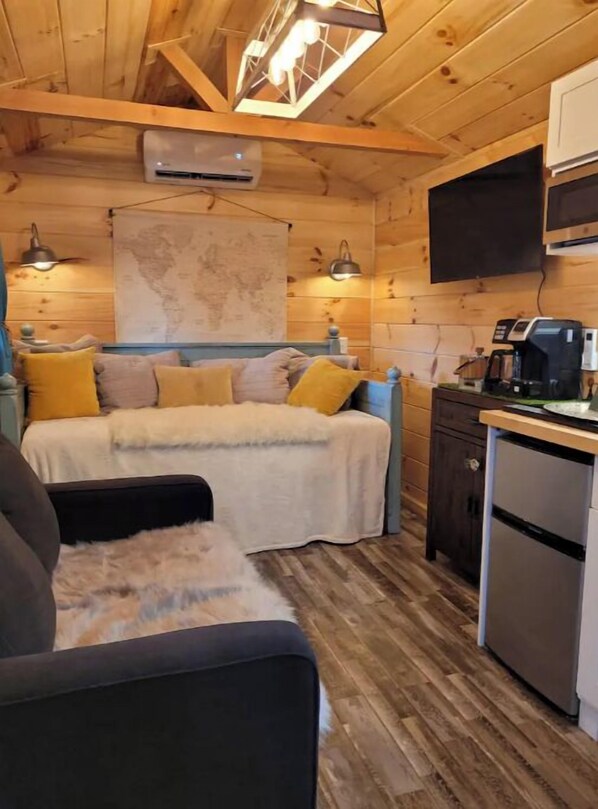 Un chalet confortable comprenant un lit, un canapé, un coin cuisine avec une machine à café et un téléviseur fixé au mur.