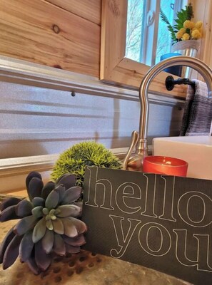 Une cuisine avec un plan de travail en bois, un évier et un panneau décoratif sur lequel on peut lire : « Bonjour ».
