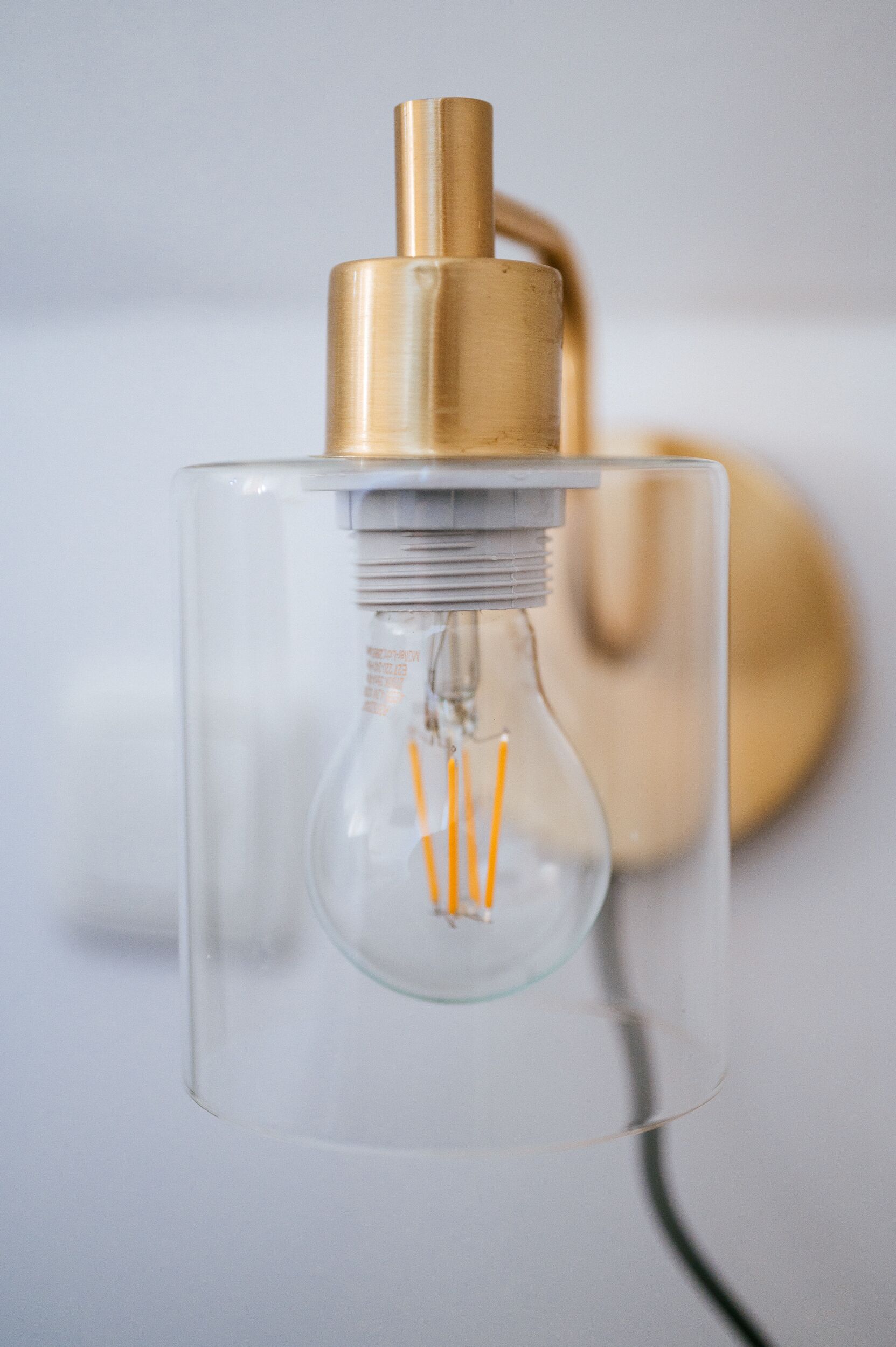 A clear glass light fixture with a gold-colored base and a visible filament inside.