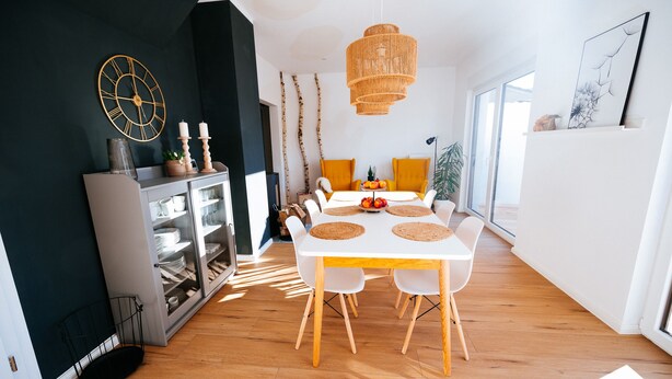 Et moderne spiseområde med et hvidt bord, træstole og et stort ur på væggen.