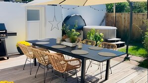 En terrasse med bord, stole, grill, jacuzzi og lyskæder.