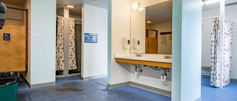 A public restroom with a blue floor, a hand dryer, a mirror, and a sign instructing to shower before entering the pool.