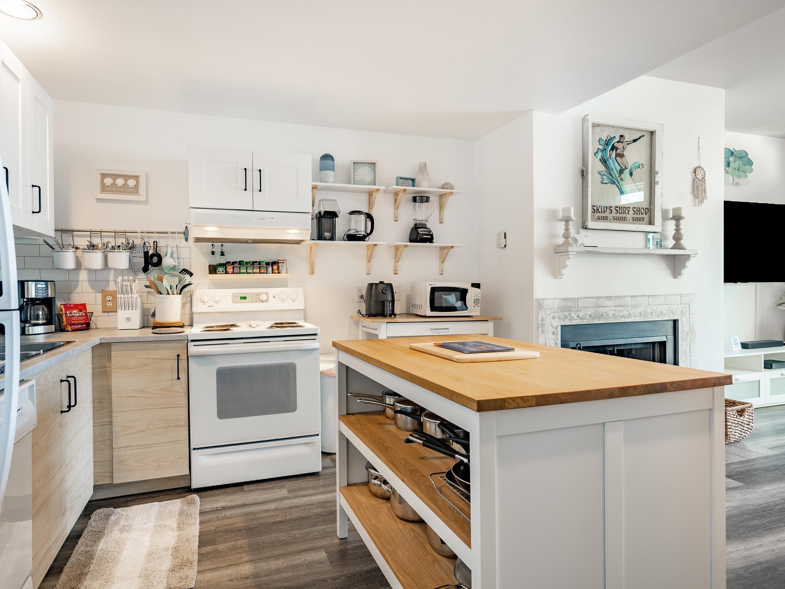 A modern kitchen with white cabinetry, a wooden countertop, and a built-in oven. There are various kitchen appliances and utensils visible.
