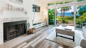 A modern living room with a fireplace, a large TV, and a view of the ocean through glass doors.