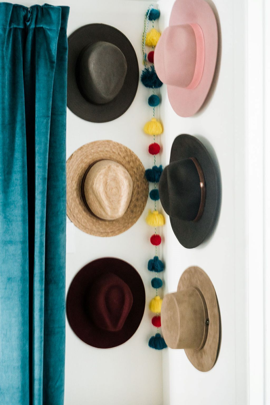Une collection de chapeaux disposés sur une surface blanche, avec un rideau turquoise visible en partie.