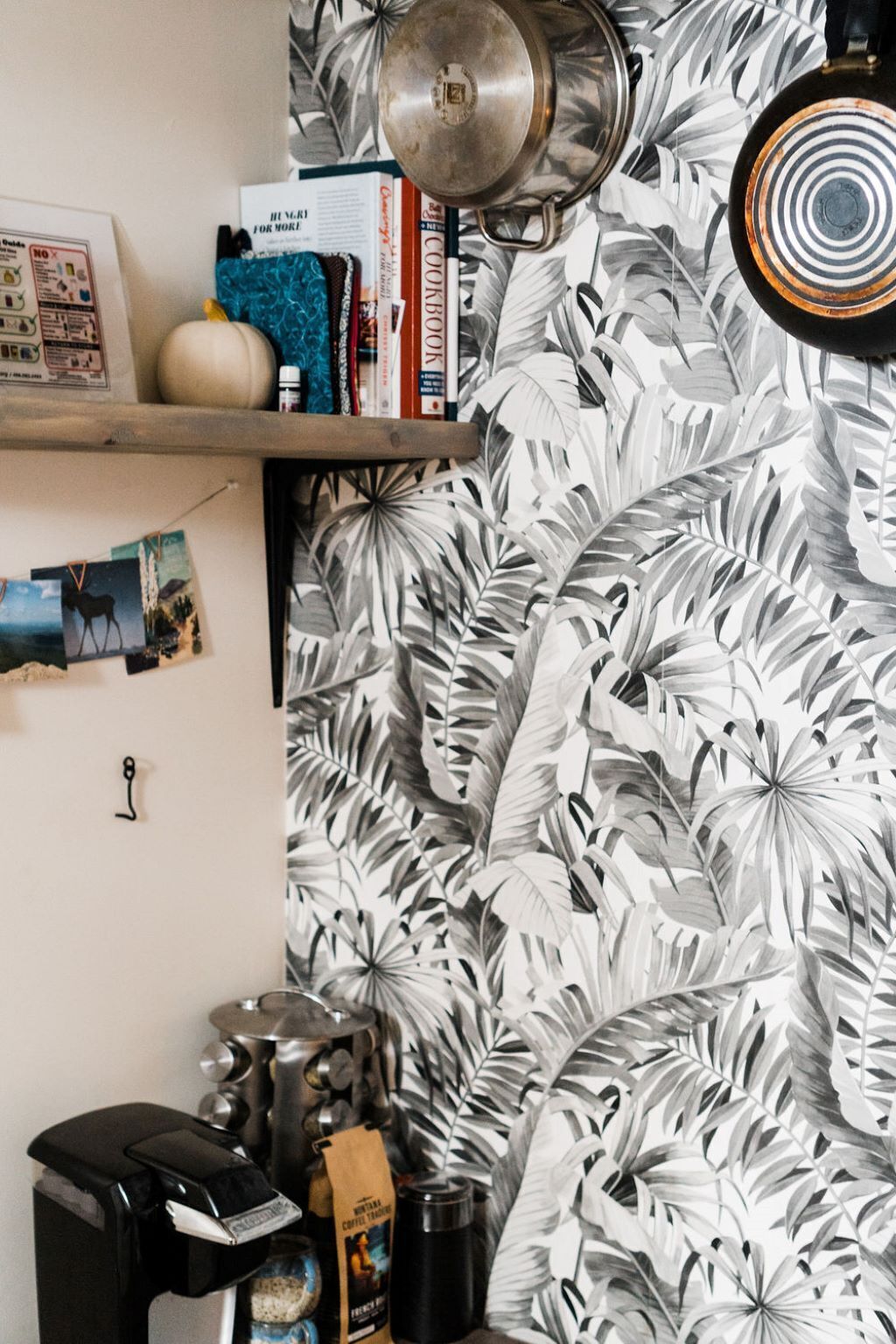 A kitchen with a tropical leaf-patterned wallpaper, a coffee machine, and various kitchen items on the counter.