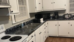 A kitchen with white cabinets, a black countertop, a stove, and a microwave.