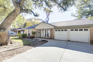 Une maison de plain-pied avec un garage, une allée et un grand arbre au premier plan.