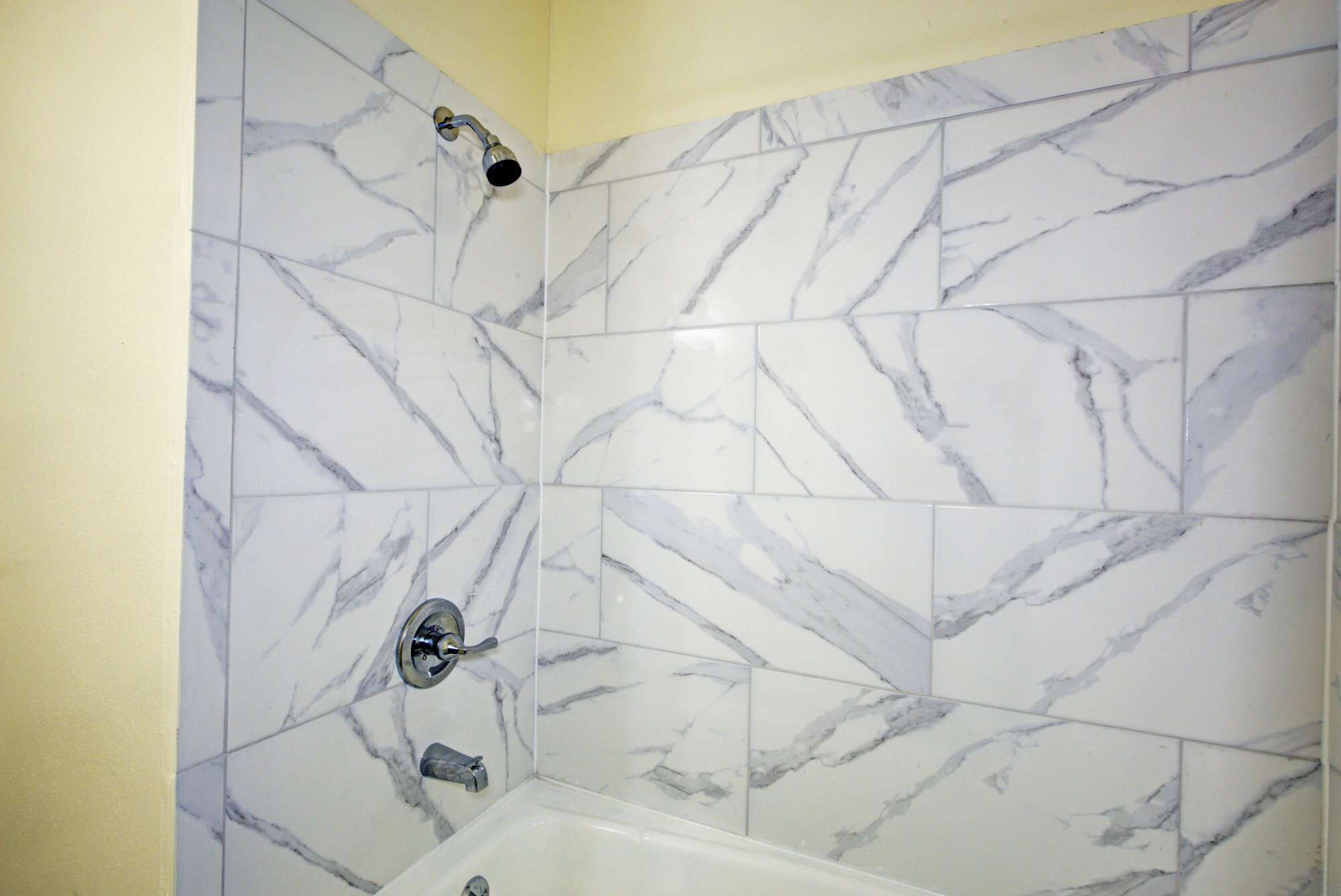 A bathroom with white marble tiles and a bathtub.