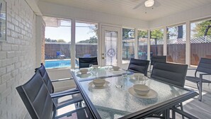 Eine überdachte Terrasse mit einem Glastisch und Stühlen, einem Deckenventilator und Blick auf einen Garten mit einem Pool.