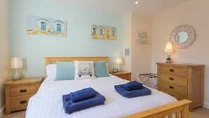 A neatly made bed with blue towels, a wooden headboard, and artwork on the walls. - Beach Walk (Chathill)