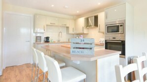 A modern kitchen with white cabinetry, a central island with bar stools, and a microwave oven. - Beach Walk (Chathill)
