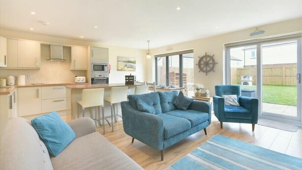 A modern living room with a sofa, a blue armchair, and a dining area with a table and chairs. - Beach Walk (Chathill)