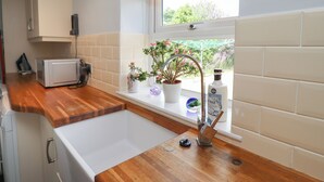 A kitchen with a wooden countertop, a white sink, and a window with a view of greenery. - Alnside Cottage (Alnwick)