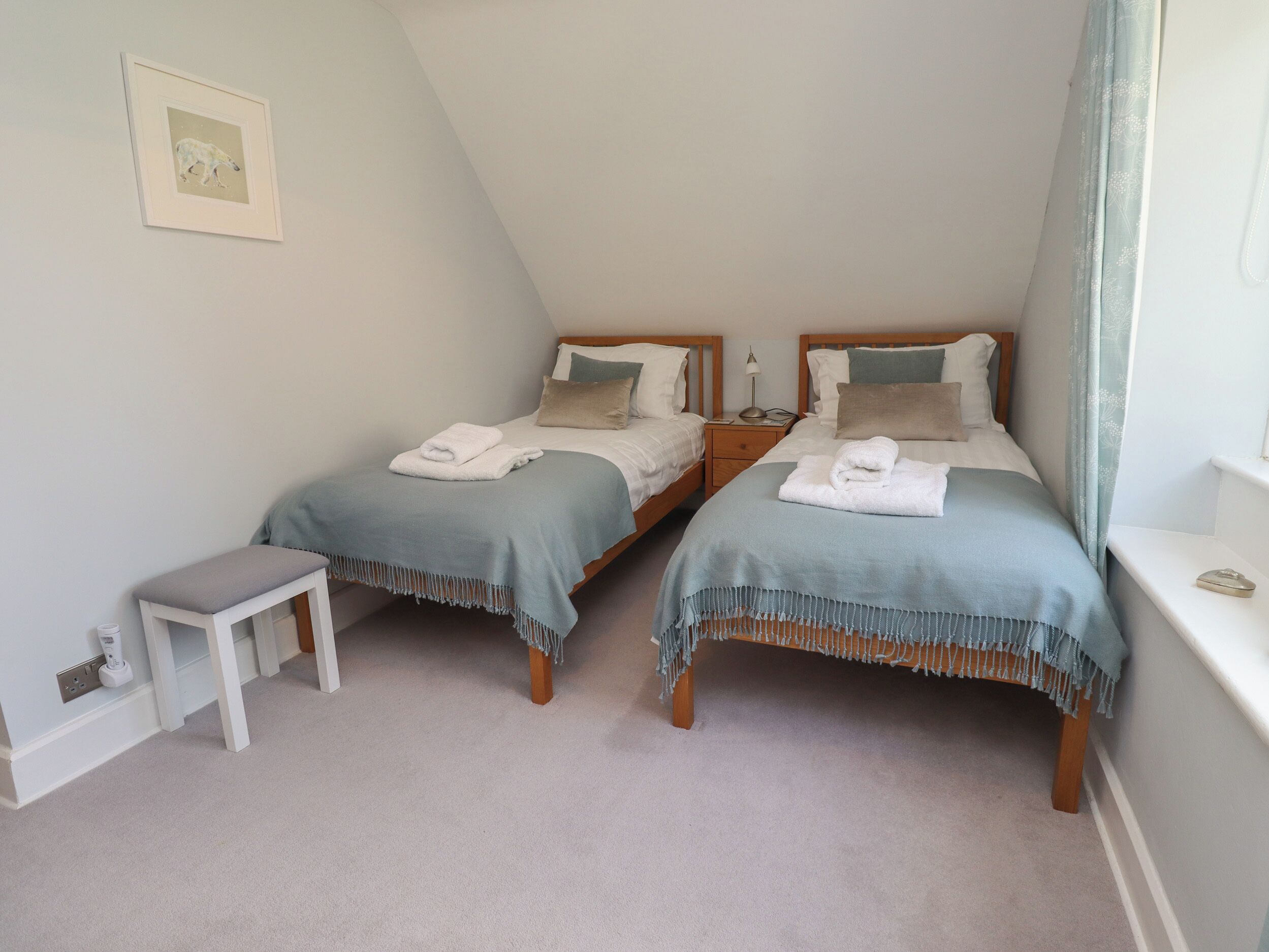 A bedroom with two beds, a bedside table, and a small bench.
