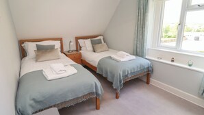 A bedroom with two single beds, a window with curtains, and a small bedside table with a lamp. - Alnside Cottage (Alnwick)