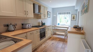 A modern kitchen with wooden flooring, white cabinetry, a gas stove, and a built-in oven. - Alnside Cottage (Alnwick)