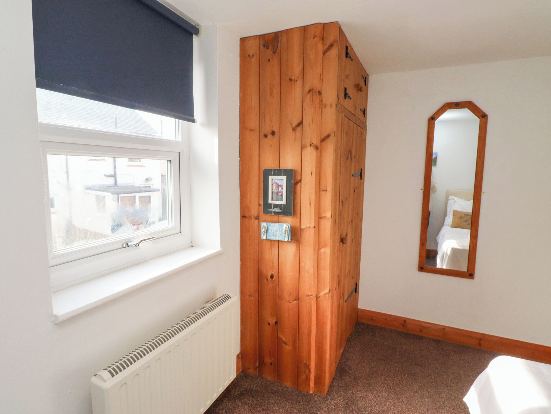 A room with a window, radiator, wooden wardrobe, and a mirror on the wall.