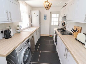 Compact kitchen with light cabinetry, black tile floor, and essential appliances.
