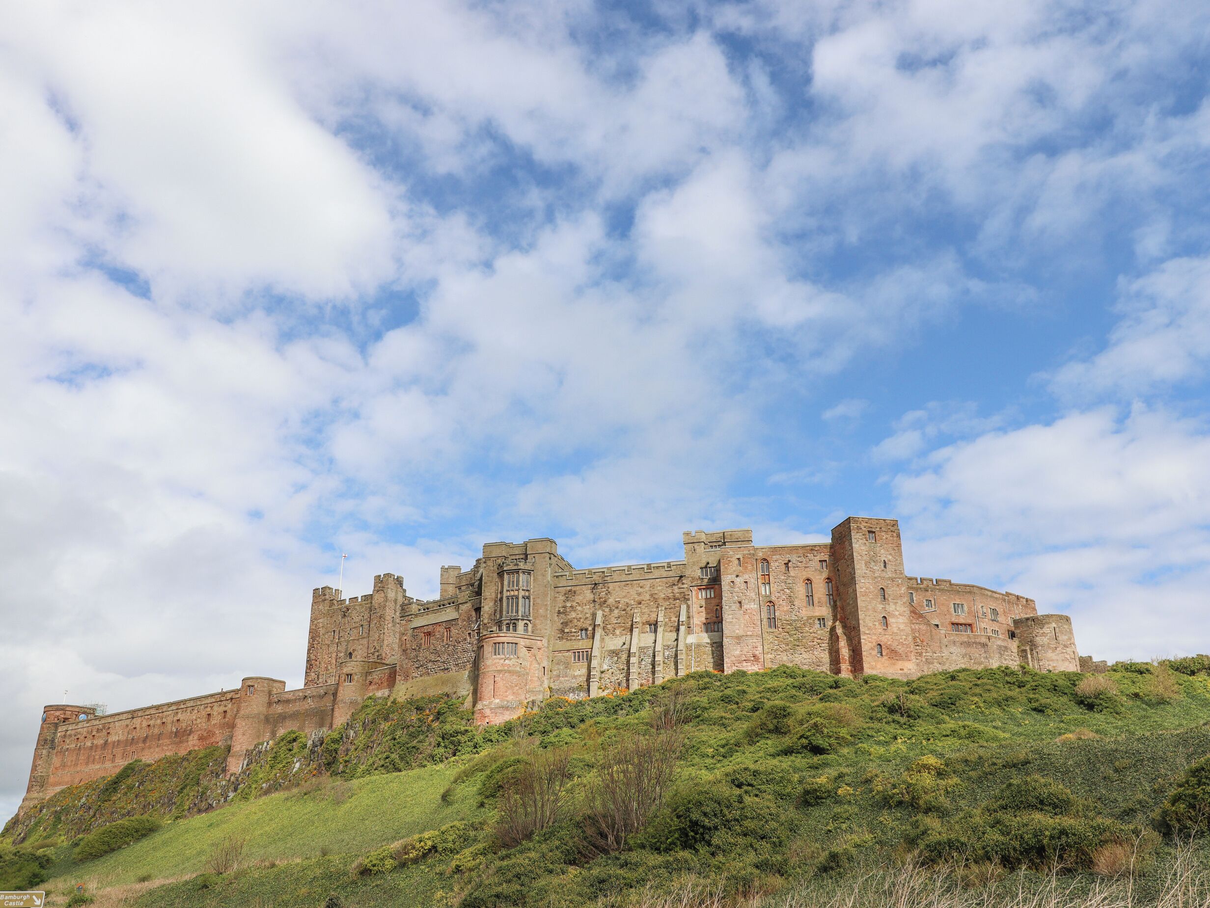 A historic castle with multiple towers and battlements, situated on a grassy hill under a partly cloudy sky.
