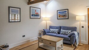 A cozy living room with a blue sofa, a wooden coffee table, and framed pictures on the wall. - Coral Cottage (Bamburgh)