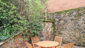 A round wooden table with four chairs, set against a stone wall and surrounded by greenery. - Coral Cottage (Bamburgh)