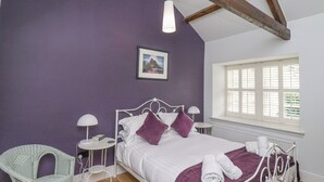 A bedroom with a bed, a chair, a table, a window, and a picture on the wall. - Coral Cottage (Bamburgh)
