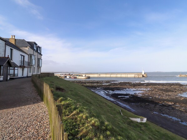 Un bâtiment situé sur la côte, avec un chemin de gravier, une zone herbeuse et une rive rocheuse.